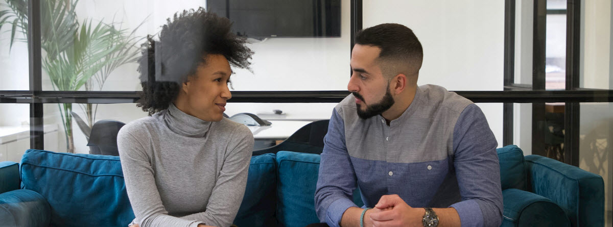 A man and a woman sitting on a coach facing each other in conversation in a workplace